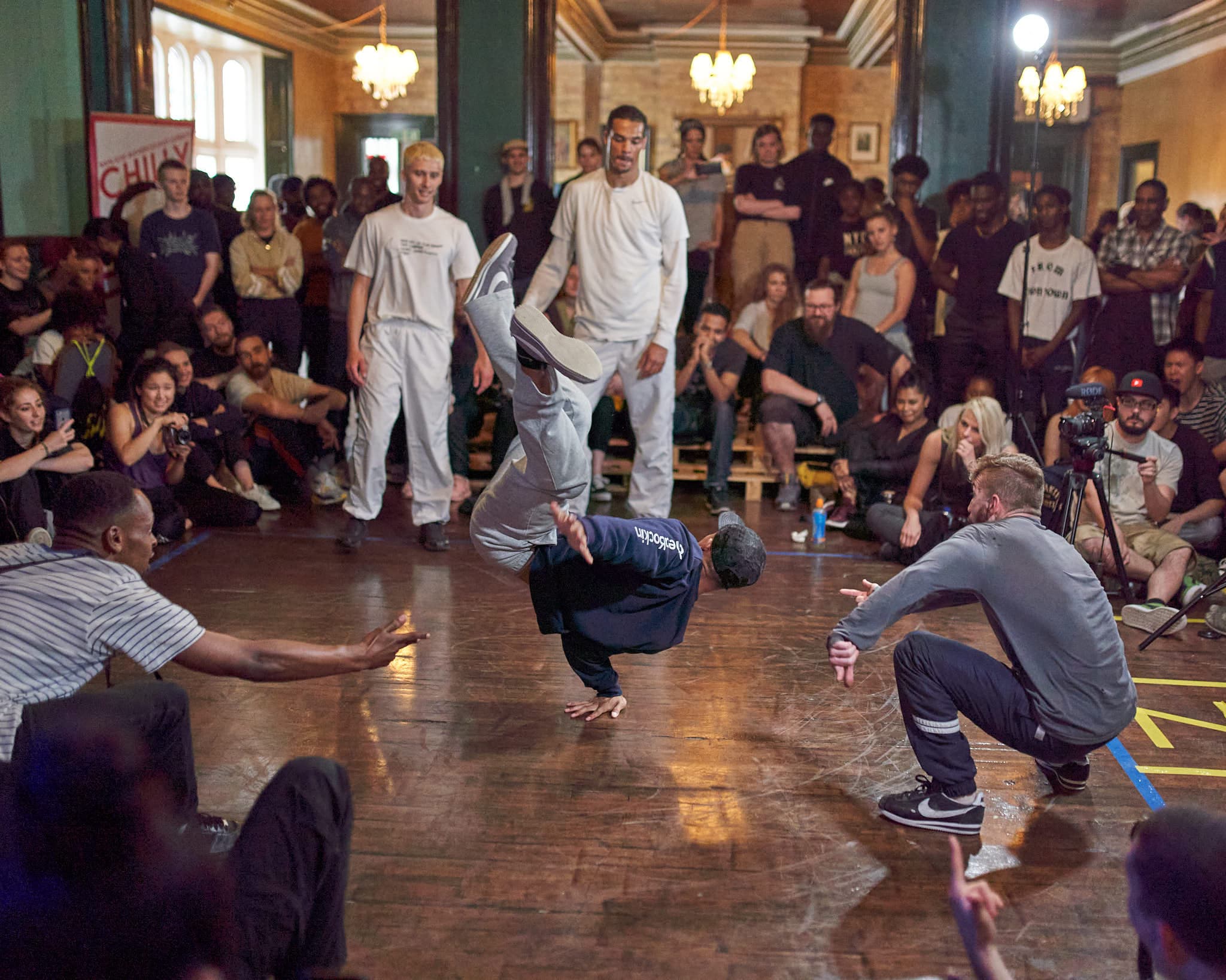 Guy break dancing in the middle of spectators and rival dancers standing close by