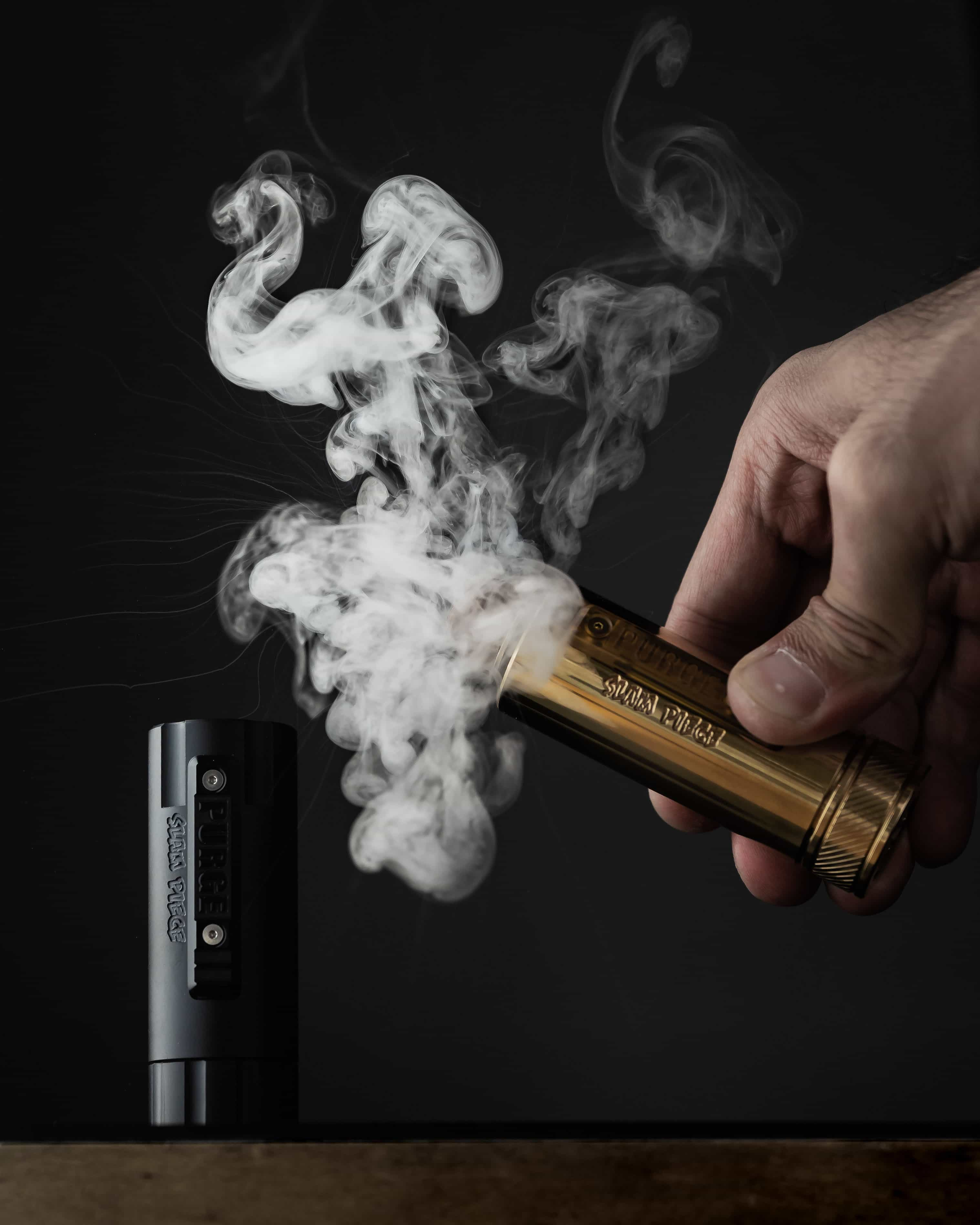 A picture of E-cigarette and a mans hand turning on the E-cigarette to let out the smoke